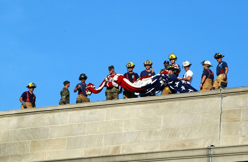 Firefighters and service members unfurling a large American flag over the side of the Pentagon on September 12, 2001